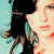 Pixelated close-up of a person with dark hair and light skin, wearing a teal garment against a pale blue background.