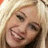 Pixelated close-up of a smiling person with light brown hair and dark eyes, wearing a dark top against a light background.