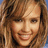 Pixelated close-up of a smiling person with light brown hair and visible teeth, set against a blurred background.