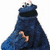 Blue furry character with black mouth and brown hand, standing against white background; red text below reads "BRING BACK THE REAL COOKIE MONSTER".