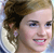 Pixelated close-up of a person with light brown hair tied back, wearing a white top with blue accents, smiling with visible teeth.