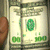 Stacks of US dollar bills held by hands, with green and white color scheme.