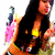 A woman with long dark hair in a yellow bikini top and green shorts poses with hands near her chest, background includes pink and blue elements.