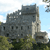 Pixelated static image of a stone castle with multiple towers under a light blue sky, surrounded by green foliage at the base.