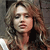 Pixelated image of a person with light brown curly hair wearing a dark top against a muted background.