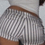 A person wearing a white top and striped shorts with visible brown belt, viewed from behind in four showing slight movement