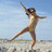 Pixelated figure in a yellow bikini performing a dynamic pose on a beach with blue sky background.