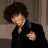 A four- animated sequence shows a person with curly brown hair in black and blue clothing, transitioning from a neutral pose to an embrace near an orange vehicle against red background