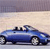 Blue convertible car with black soft top and black roof supports, viewed from side against light background.