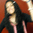 A person with long dark hair and a black cardigan over pink clothing appears in four against a reddish-brown background, showing slight variations in pose