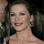 A pixelated close-up of a person with dark hair, wearing a strapless top and a small earring, smiling with visible teeth and red lipstick.