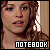 Pixelated close-up of a person with brown hair and light skin, wearing a dark top, with the word 'NOTEBOOK' in white block letters at the bottom.