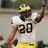 A football player in a white jersey with number 20 and yellow pants raises one arm while wearing a yellow helmet.
