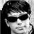 Black-and-white pixelated icon of a person wearing dark sunglasses with short hair, rendered in low-resolution grayscale with visible dithering and anti-aliased edges on the face and hair.