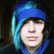 Pixelated close-up of a person wearing a blue hooded garment with light blue accents, set against a dark background.