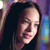 Pixelated close-up of a person with long dark hair, light skin, and pink lips, set against a blurred multicolored background.