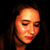 Pixelated close-up of a person's face with closed eyes, warm orange and brown tones, dark background, and visible hair strands.