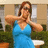 A static pixelated image shows a person in a blue sleeveless dress with arms extended horizontally, standing before a blurred background of greenery and light-colored structures.