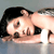 Pixelated image of a person with dark hair lying on their back, eyes closed, mouth open, and arms raised above the head against a gray background.