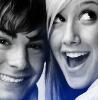 Two people in close proximity, one with dark hair and the other with light hair, both smiling broadly with open mouths showing teeth.