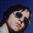 Pixelated static icon of a person with dark hair and sunglasses against a blue background, rendered in low resolution with visible dithering and color blending.