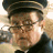 Pixelated static image of a person wearing a dark cap and glasses, with light-colored hair visible beneath the cap, set against a blurred background.