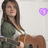 A person with long brown hair wearing a green top and white undershirt holds a brown guitar against a light background with a heart symbol changing color.