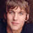 Pixelated portrait of a person with light brown hair against dark background, adjacent to blue with text and symbol