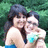 Two people embrace outdoors; one wears a blue strapless top, the other a light blue top with green accents, against a green foliage background.
