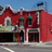 Static pixelated image of a red brick building with dark windows and a blue sky background.