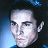 Pixelated close-up of a person's face with dark hair, light skin, and visible eyes, nose, and mouth against a blue and black background.