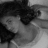 A grayscale pixelated image of a person with dark hair, a light-colored top, and a blurred background, appearing to be a low-resolution digital portrait.
