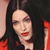 A pixelated close-up of a person with long dark hair, red lips, and a red garment against a dark background.