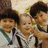 Three children in school uniforms pose together with a baby, surrounded by pink pixelated text reading "Can you imagine... These cuties are the one the only... Jonas Brothers!!!".
