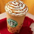 A pixelated close-up of a Starbucks drink with whipped cream and chocolate drizzle, held by hands in red fabric.