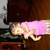 A pixelated figure in a pink outfit lies on a dark surface with a light-colored background, viewed from above.