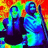 Two figures in dark clothing stand against a red and green pixelated background; one figure holds a long object while the other raises a hand to their face.
