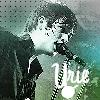 Pixelated image of a person with dark hair holding a microphone, wearing a shirt with 'Unie' text, against a gradient background.