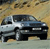 Pixelated image of a dark-colored pickup truck with a white front section, positioned on a textured ground against a gradient background.