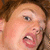 A pixelated close-up of a person's face showing light skin, brown hair, and a slightly open mouth with visible teeth.