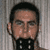 Static pixelated image of a person's face with dark hair and glasses against a gray background, rendered in low-resolution style typical of early 2000s digital art.