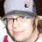 Pixelated image of a person wearing a gray cap with a small logo, glasses, and a white shirt with red accents, set against a red background with text.