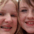 A static image of two smiling people with light brown hair, cropped closely to show only their upper faces and shoulders.