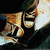 Pixelated static image of a character with dark hair and glasses holding a golden trophy against a gradient background.