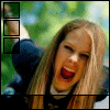 A static image of a person with long blonde hair and red lipstick, wearing dark clothing against a blurred green background.