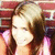 Pixelated image of a person with light-colored hair and dark brown hair sections, wearing pink clothing against a red background.