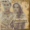 Two people pose together with a heart-shaped gesture, one holding a microphone, against a textured background with the word 'hollister' visible.