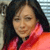 A pixelated close-up of a person with long dark hair wearing a red and pink garment against a blurred background.