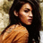Pixelated static image of a person with long dark hair wearing a light brown sleeveless top against a blurred background.