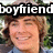 Pixelated image of a smiling person with light brown hair, wearing a blue shirt under green foliage background and overlaid black text reading 'boyfriend'.